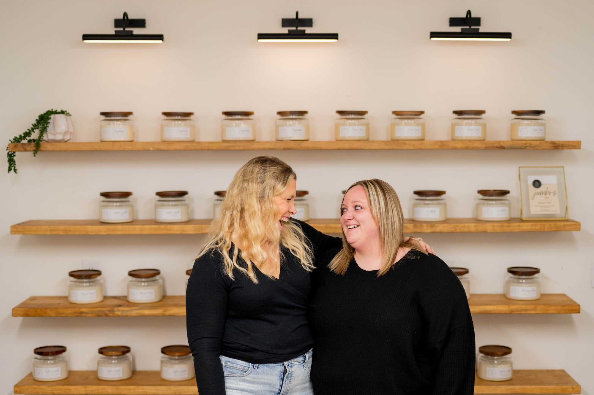Two women standing in front of shelves with jumbo candles on a white wall.