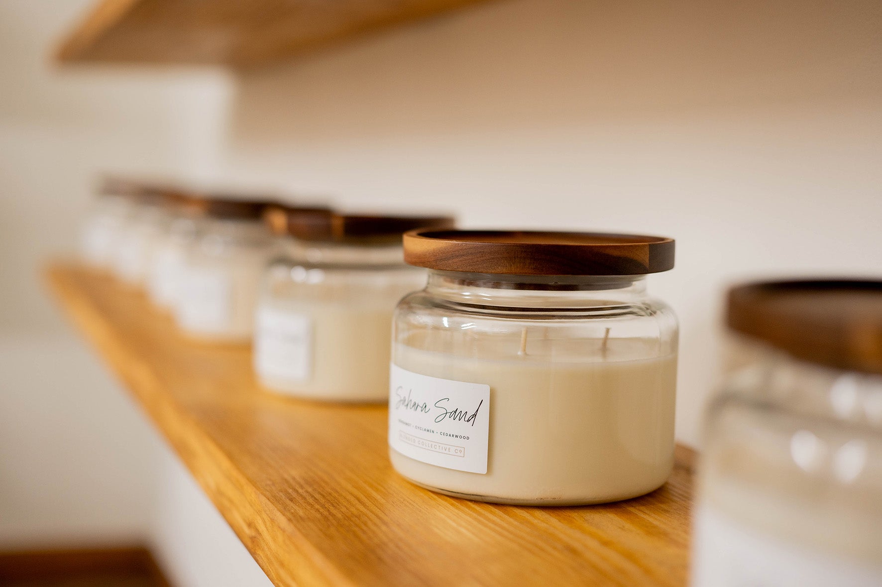 Row of candles in glass jars with wooden lids on a wooden shelf.